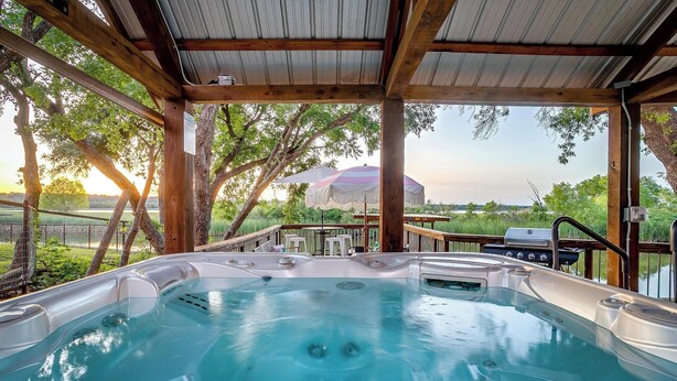 Ein Whirlpool unter einer Holzpergola mit Blick auf Bäume und einem Grillbereich.