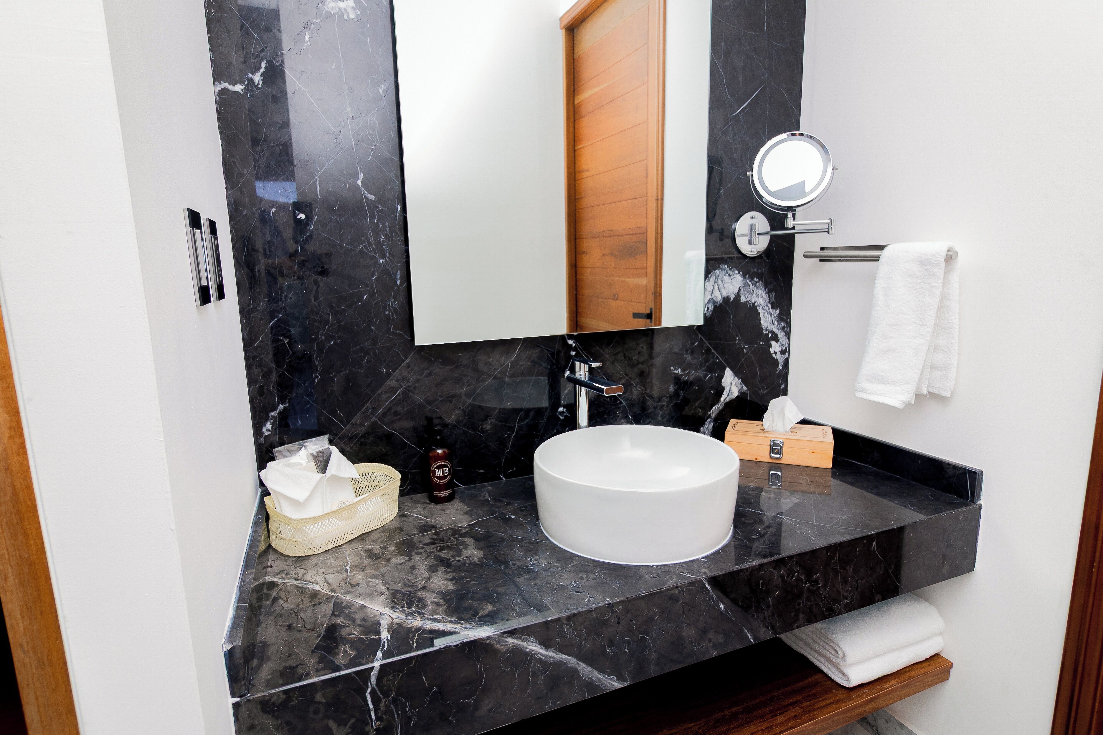 Un baño con encimera de mármol, lavamanos blanco, puerta de madera, espejo y toallero.