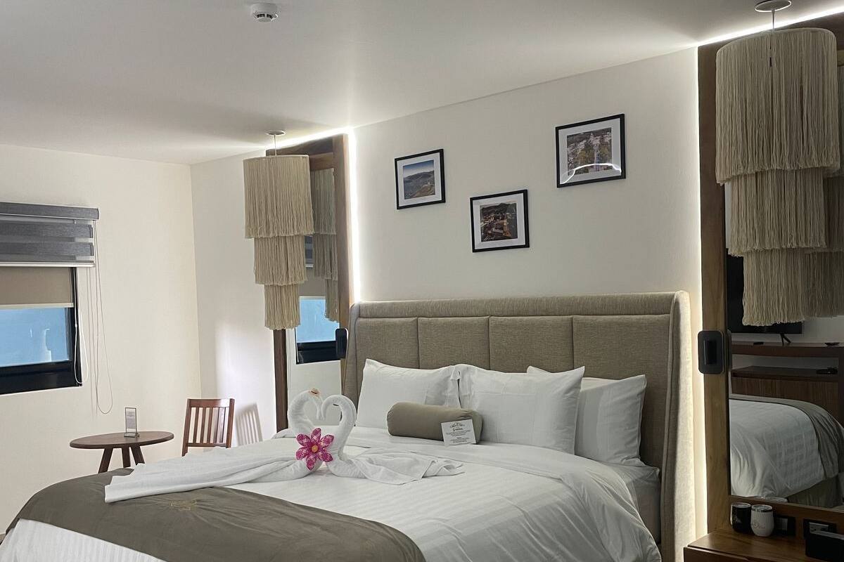 A modern hotel room with a large bed, a round table, and a chair. There are three framed pictures on the wall.