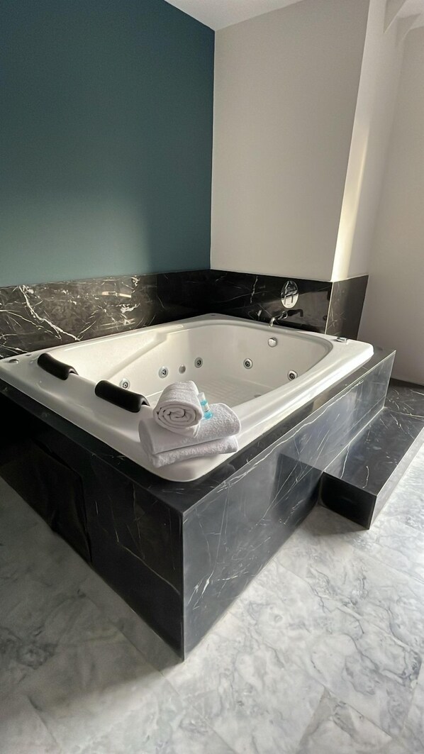 A modern bathroom with a black marble bathtub, a white towel, and a glass shower enclosure.