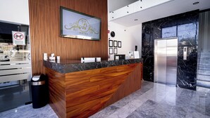 A hotel reception desk with a wooden finish, a framed sign above it, and a marble floor. - Hotel Guiant (Santa María del Río)