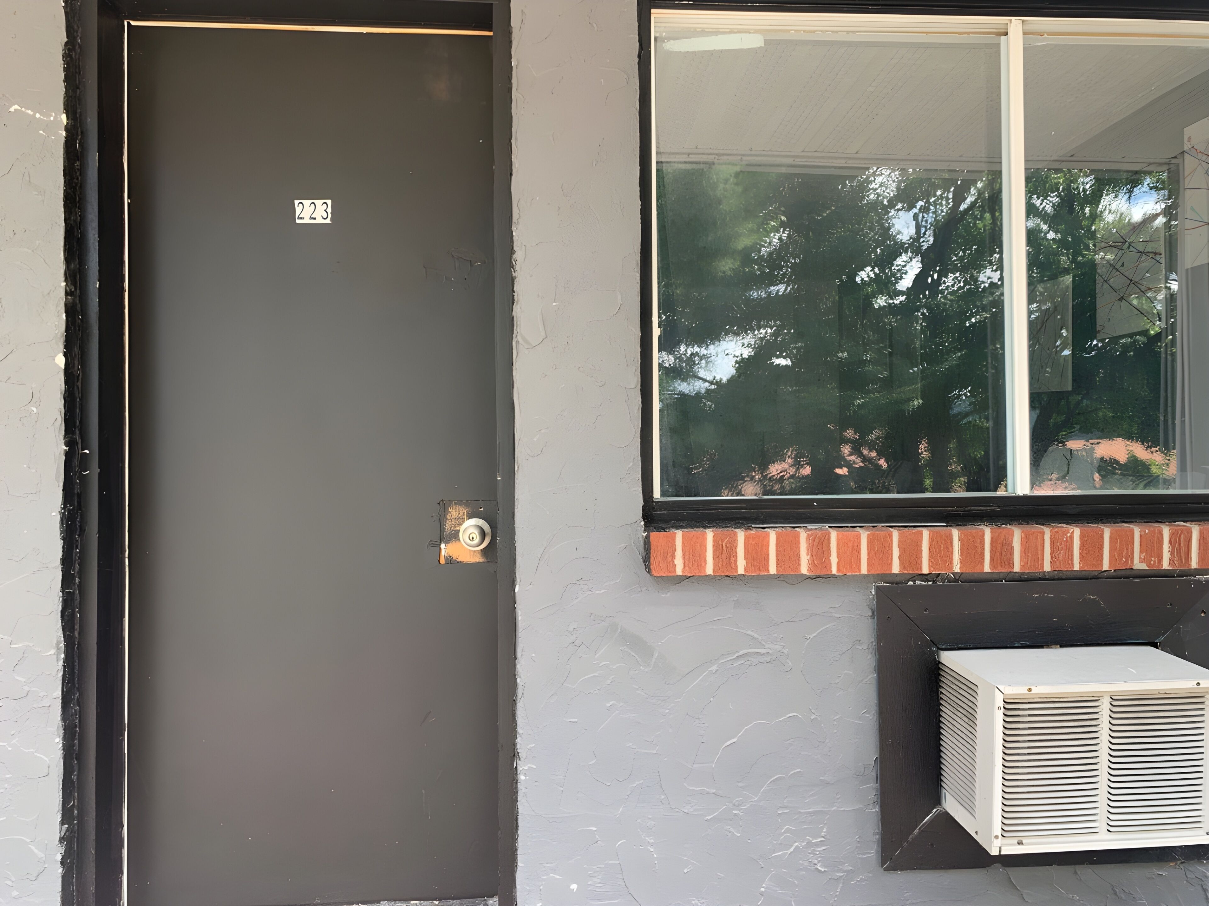 A door with a number, a window with a view of trees, and an air conditioning unit.