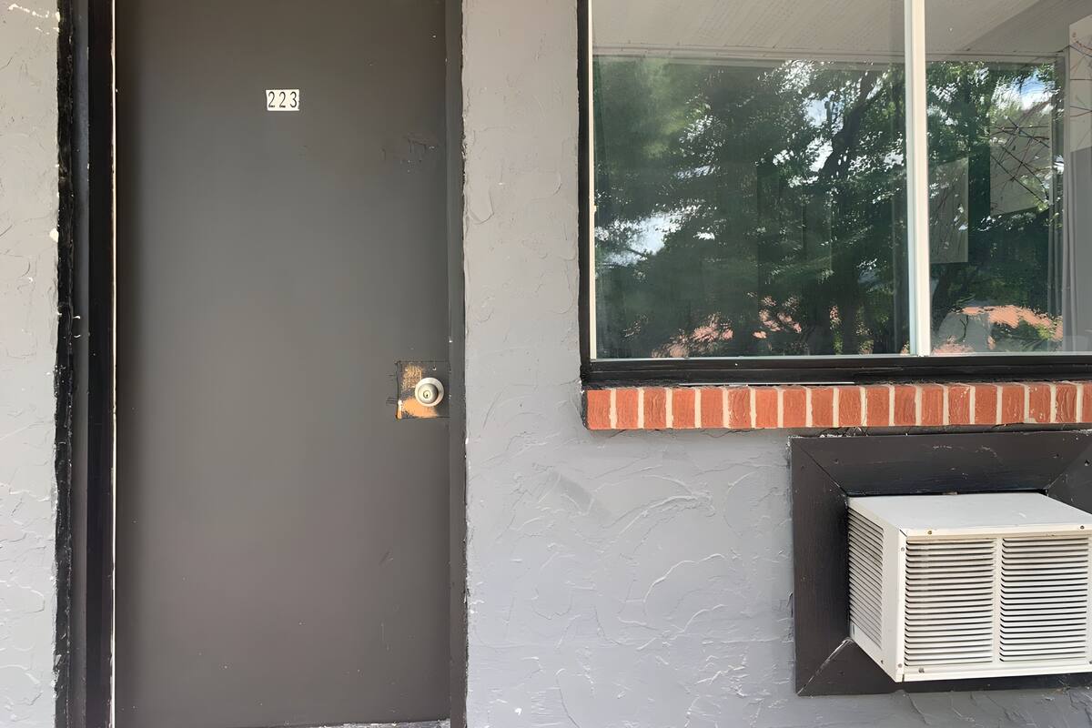 A door with a number, a window with a view of trees, and an air conditioning unit.
