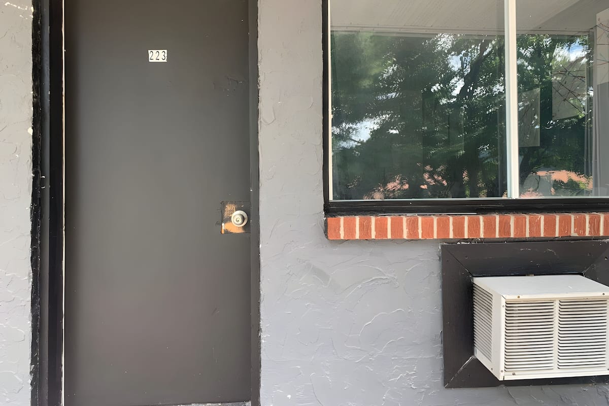 Une porte avec un numéro, une fenêtre donnant sur des arbres et un appareil de climatisation.
