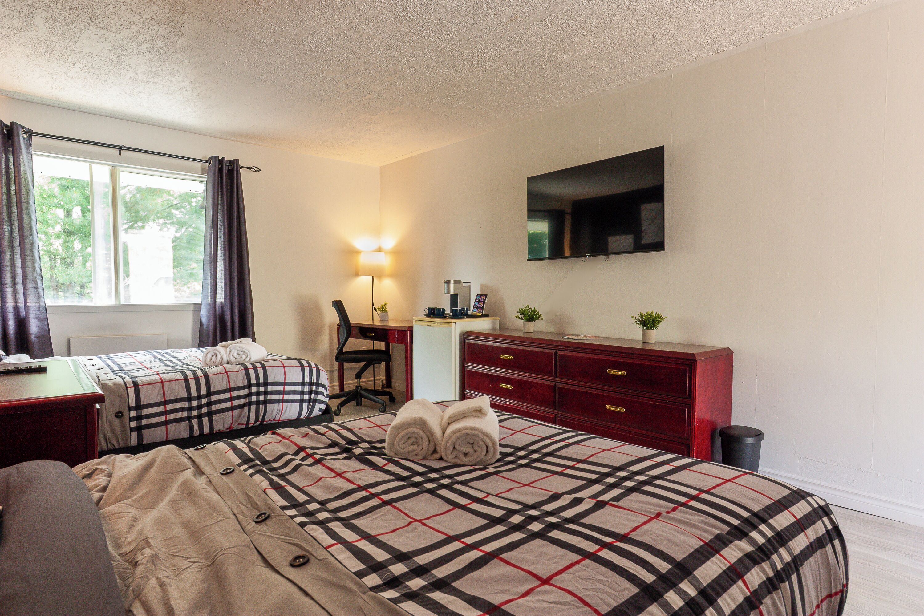 A hotel room with two beds, a desk, a chair, a TV, and a desk lamp.