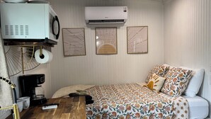 A compact room with a bed, a desk with a coffee machine, an air conditioner, and a sink. - Sunnyside Suit, Luxe Tiny Home Gulfport, MS (Gulfport)