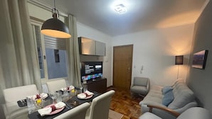 Una sala de estar moderna con comedor. Hay un televisor de pantalla plana montado en la pared, un sofá y una mesa de comedor puesta con vasos y platos.