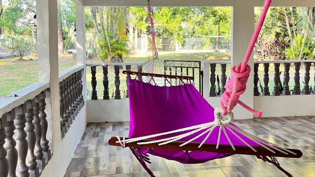 Quarto com uma rede pendurada, varanda com guarda-corpo e vista para o verde lá fora.