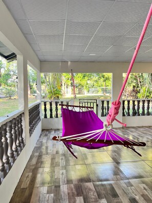 A room with a hanging hammock, a balcony with a balustrade, and a view of greenery outside. - Mi Casita del Bosque - El Higo Ideal lodging to disconnect. (Cochea)