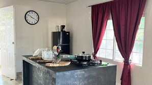 Uma cozinha com bancada preta, um relógio, uma geladeira e uma janela com cortinas vermelhas.