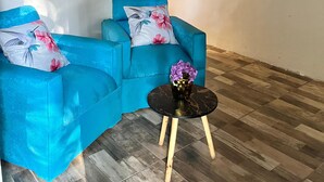 Uma sala de estar moderna com um sofá azul, uma mesa redonda pequena com um vaso e piso de madeira.