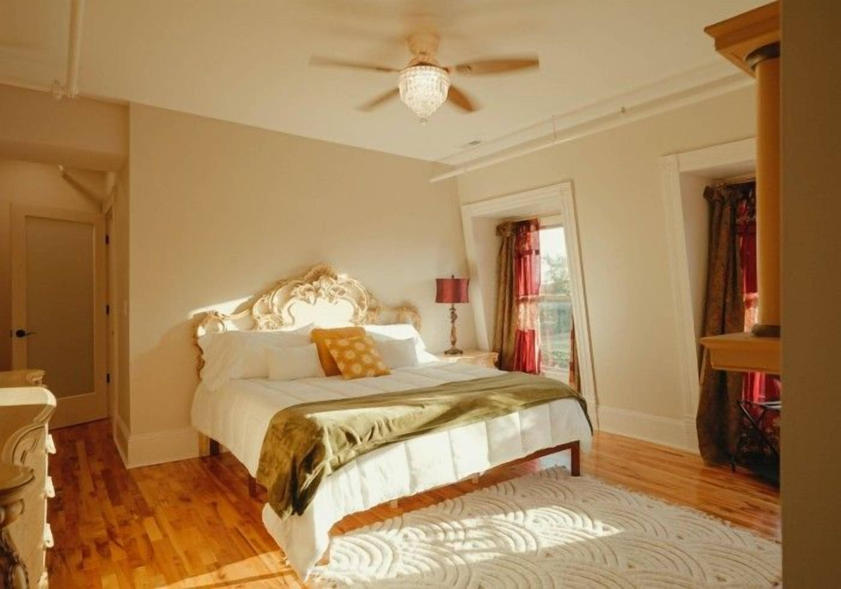 A bedroom with a bed, a ceiling fan, a window with curtains, and a wooden floor.