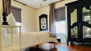 Een slaapkamer met een bed, een witte nachtkastje, een donker houten garderobe en een raam met gordijnen.