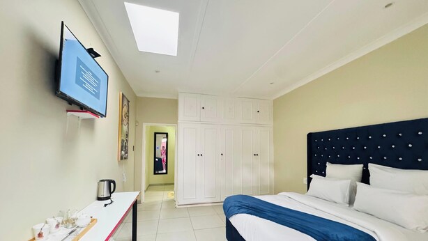 Una habitación de hotel con cama, escritorio con una bandeja de objetos, televisión y armario.