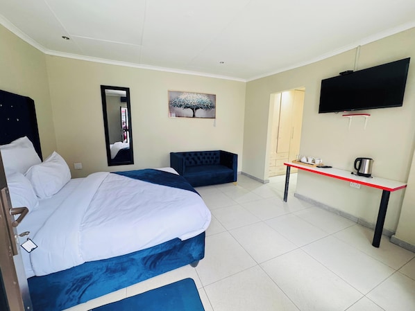A hotel room with a bed, a sofa, a TV, and a small table with a kettle.