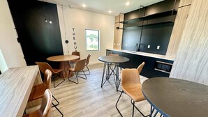 A modern kitchen with black cabinets and a wooden countertop. There are two dining tables with chairs, and a window with a view of trees. - The Hub 3b Close to Disney Gameroom (Kissimmee)