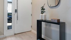 A modern hallway with a white door, a console table with a mirror, and a plant. - The Hub 3b Close to Disney Gameroom (Kissimmee)