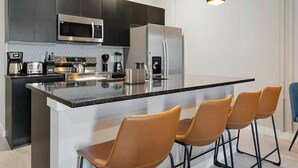 A modern kitchen with a central island, stainless steel appliances, and black pendant lighting. - The Hub 3b Close to Disney Gameroom (Kissimmee)