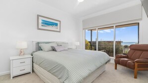 A bedroom with a large bed, a nightstand, a chair, and a view of the sea through a balcony. - Kookaburras Perch - McCrae (McCrae)