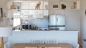 A compact kitchen with white cabinetry, a stainless steel refrigerator, a microwave, and a stove. There is a dining table with chairs and a decorative vase on the counter. - Kookaburras Perch - McCrae (McCrae)