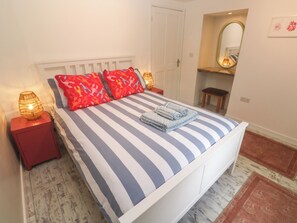 A bed with striped bedding, two red pillows, and a folded towel. There are two bedside lamps on wooden nightstands. - The Packing House (Penzance)
