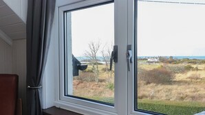 A room with a large window overlooking a grassy area and a body of water. - Cuillin View House (Arisaig)