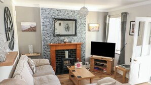 A living room with a stone fireplace, a sofa, a television, and a wooden coffee table. - Cuillin View House (Arisaig)