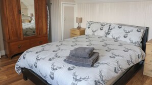 A bedroom with a bed featuring a deer print duvet, a wooden wardrobe, a mirror, and a nightstand with a lamp. - Cuillin View House (Arisaig)