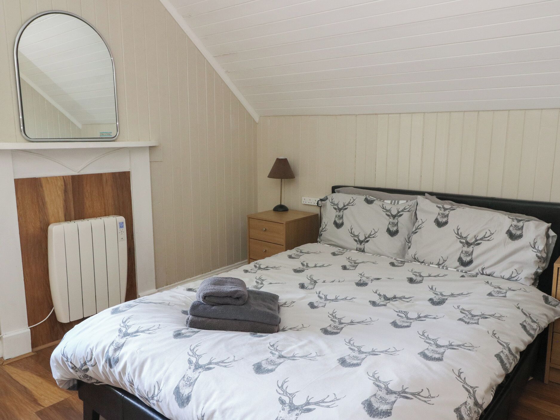 A bedroom with a bed, a nightstand, a lamp, a radiator, and a mirror.