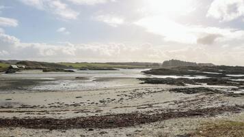 Un paisaje costero con una playa arenosa, afloramientos rocosos y un edificio pequeño a lo lejos.
