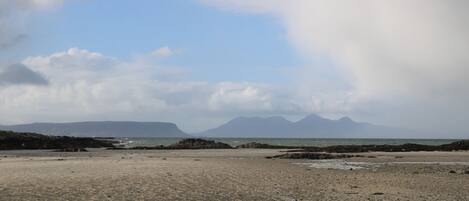 A beach with rocky terrain and distant mountains under a cloudy sky.