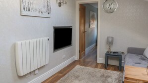 Ein modernes Wohnzimmer mit Fernseher, Heizkörper, einer Uhr und einem gemütlichen Sofa.
