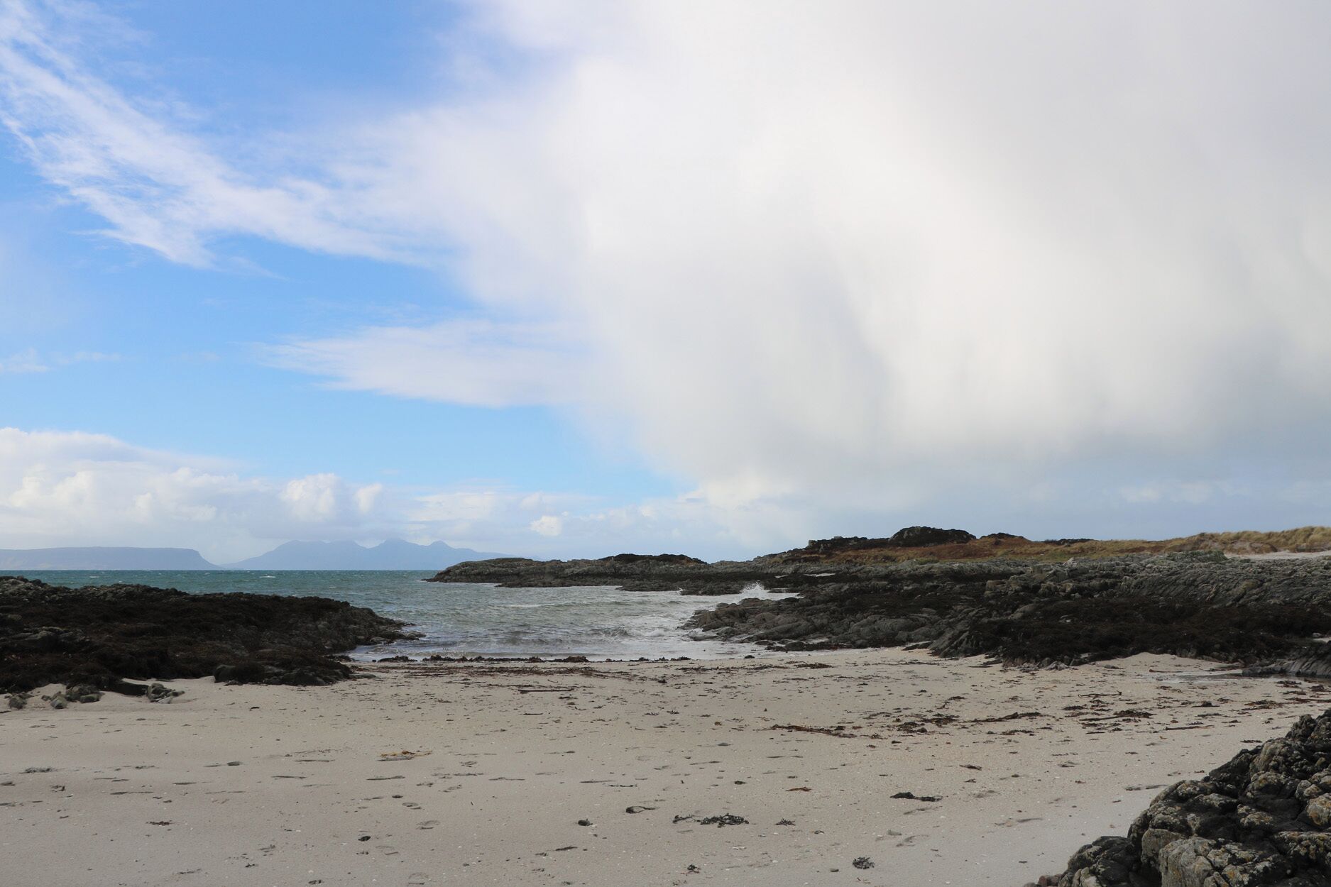 A beach with rocky outcrops and a clear sky.