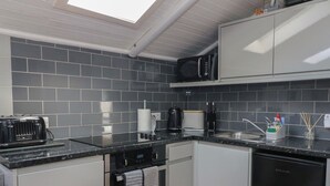 Eine kleine Küche mit grauen Fliesen an der Spritzschutzwand, einer schwarzen Mikrowelle, einem Toaster, einer Kaffeemaschine und einem Spülbecken mit modernem Wasserhahn.