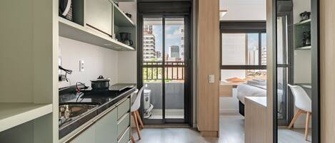 A modern kitchen with a built-in stove, a sink, and a countertop. There is a sliding glass door leading to a balcony with a view of the city.