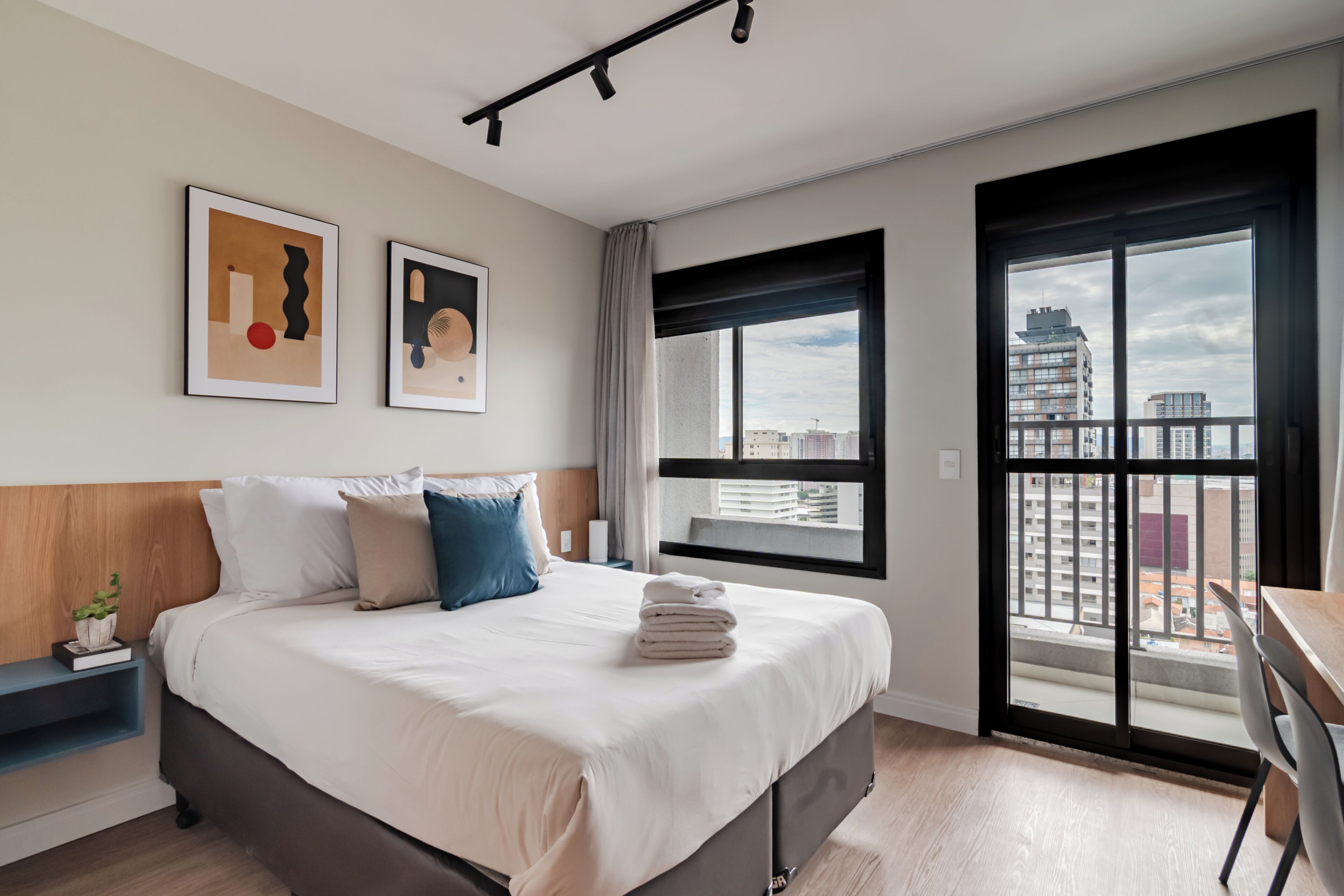 Ein modernes Hotelzimmer mit einem großen Bett, einem Schreibtisch und Blick auf die Stadt durch ein großes Fenster.