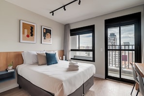 A modern hotel room with a large bed, a desk, and a view of the city through a large window. - 360 Coraz Perdizes (Sao Paulo)