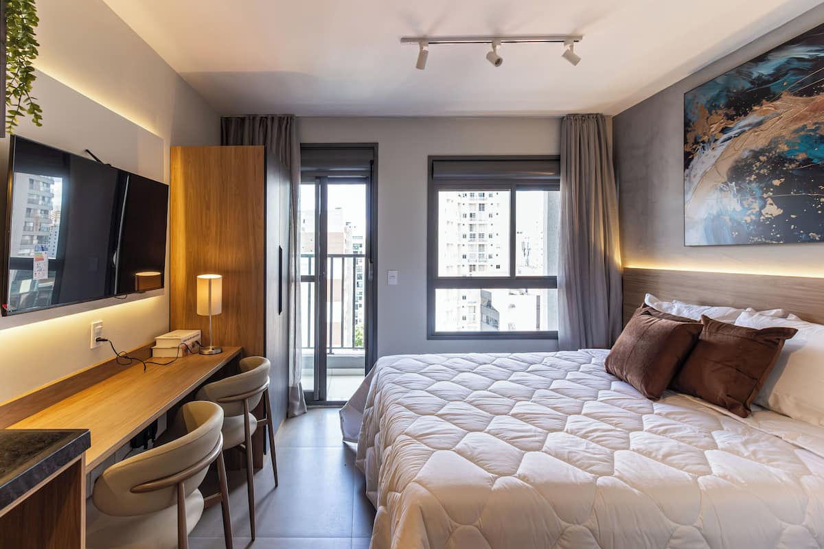 A hotel room with a bed, a desk with chairs, a TV, and a large window.