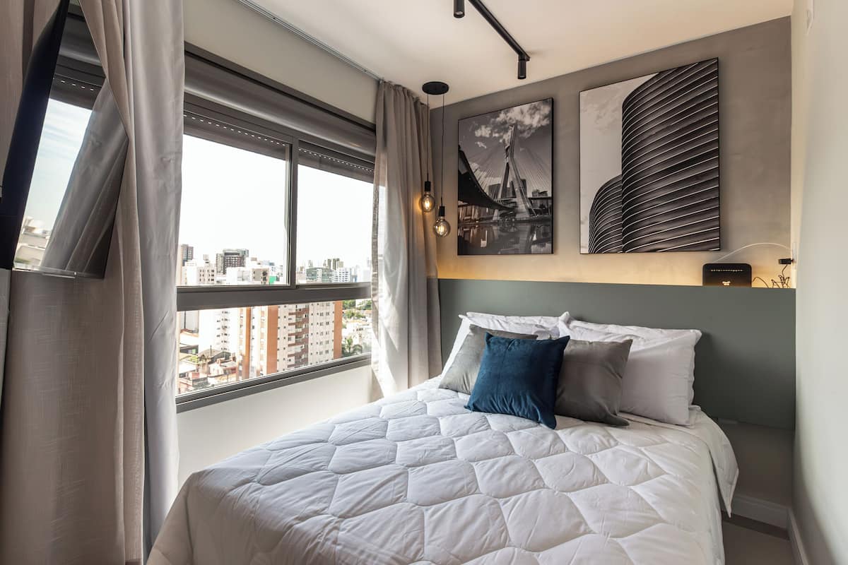 A modern hotel room with a large bed, a city view through the window, and a wall-mounted artwork.