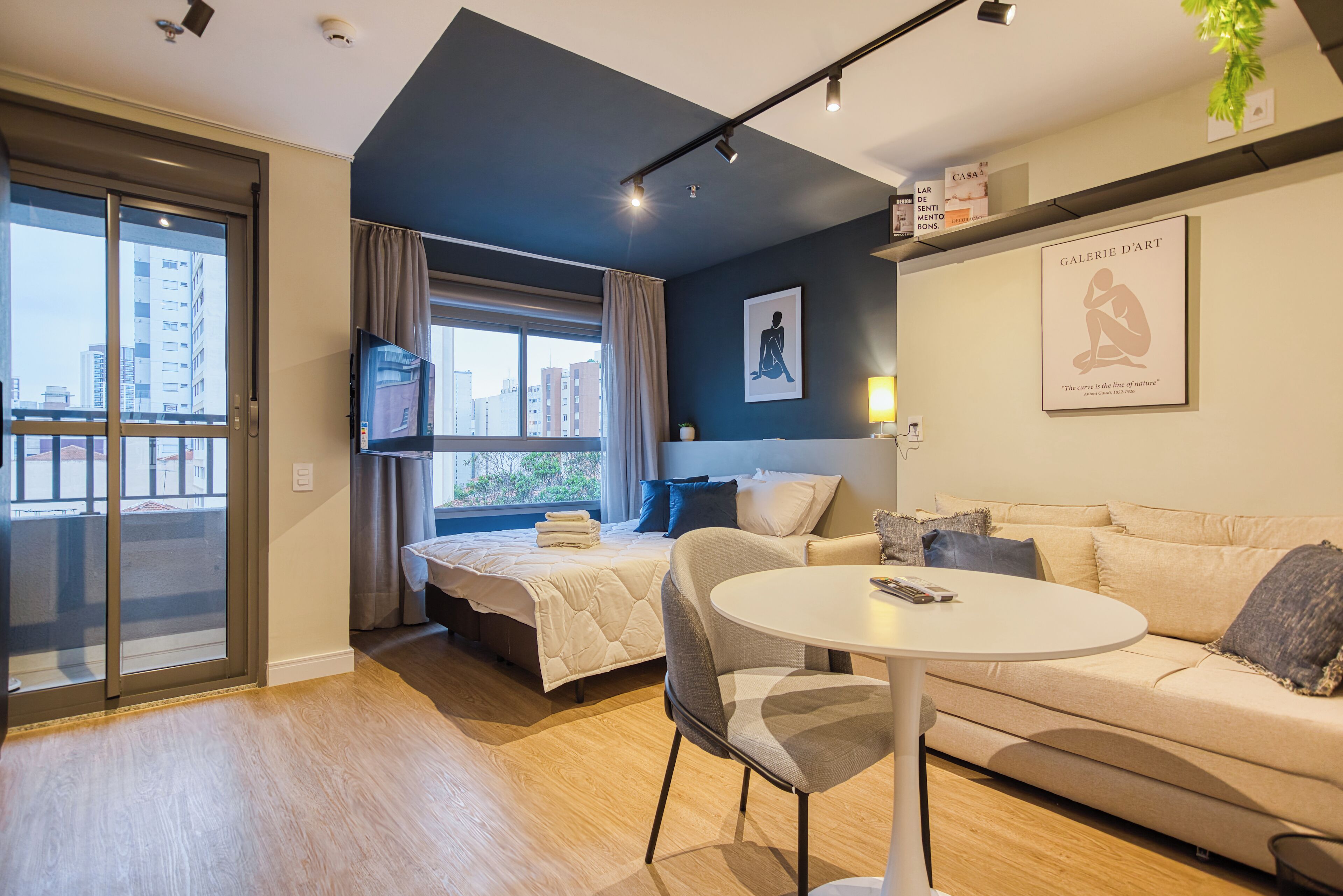 A modern hotel room with a bed, a sofa, a small table, and a TV.