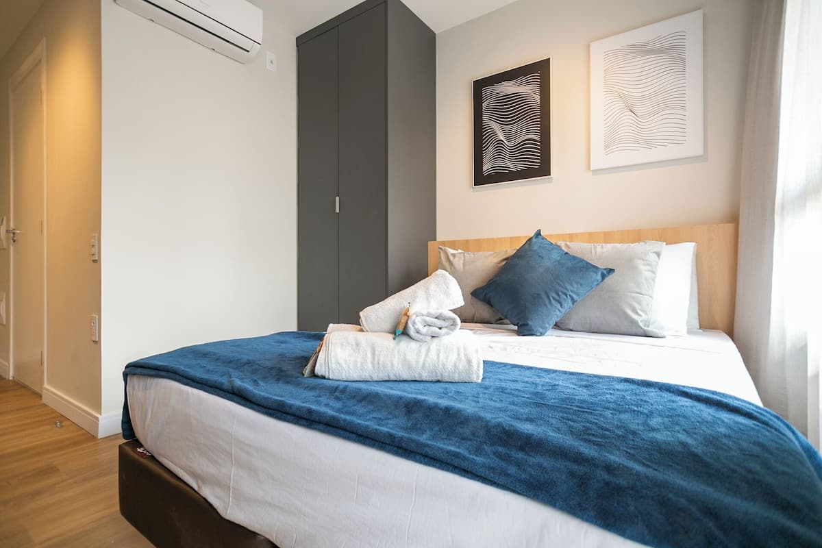 A neatly made bed with a blue blanket and white pillows, a wooden headboard, and two abstract wall art pieces.