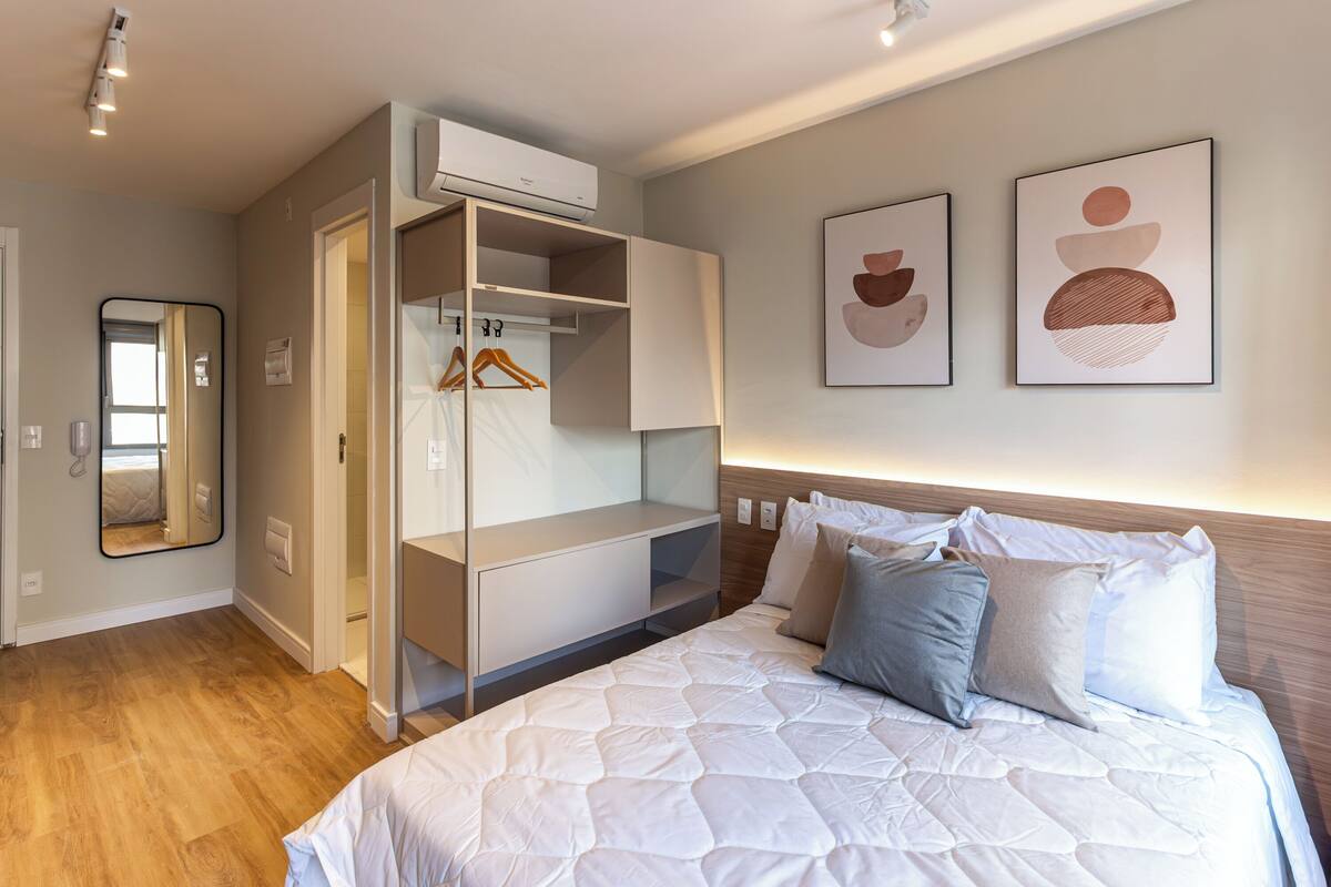 A bedroom with a bed, a wardrobe, a mirror, and two wall art pieces.
