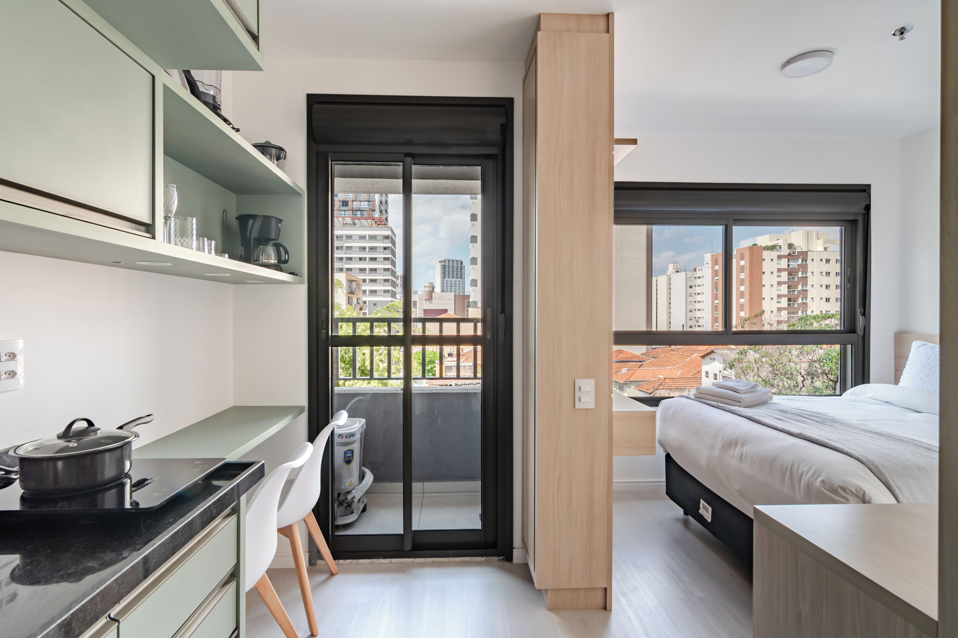 A modern bedroom with a bed, a desk, and a view of the city through a large window.