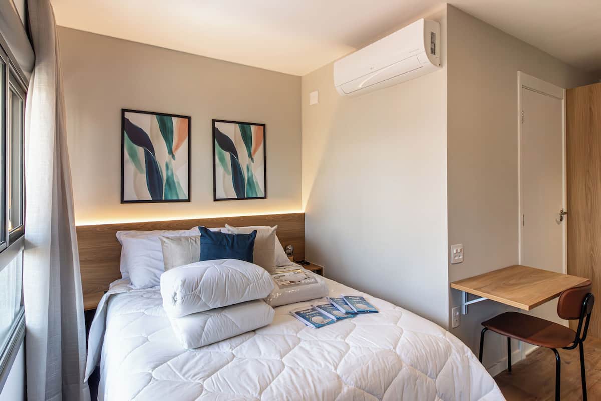 A hotel room with a bed, a desk, and two abstract paintings on the wall.