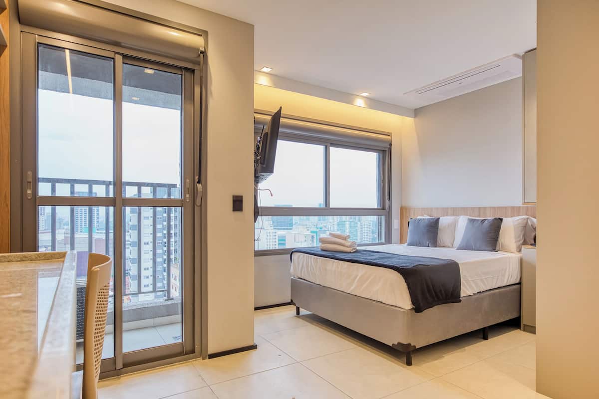 A modern hotel room with a bed, a desk, and a large window offering a city view.