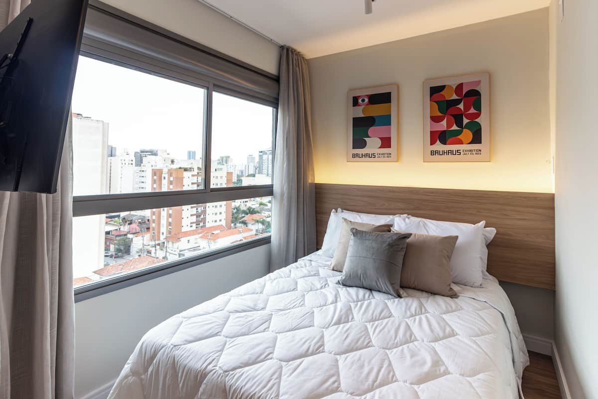 A hotel room with a large bed, a TV, and two framed artworks on the wall.