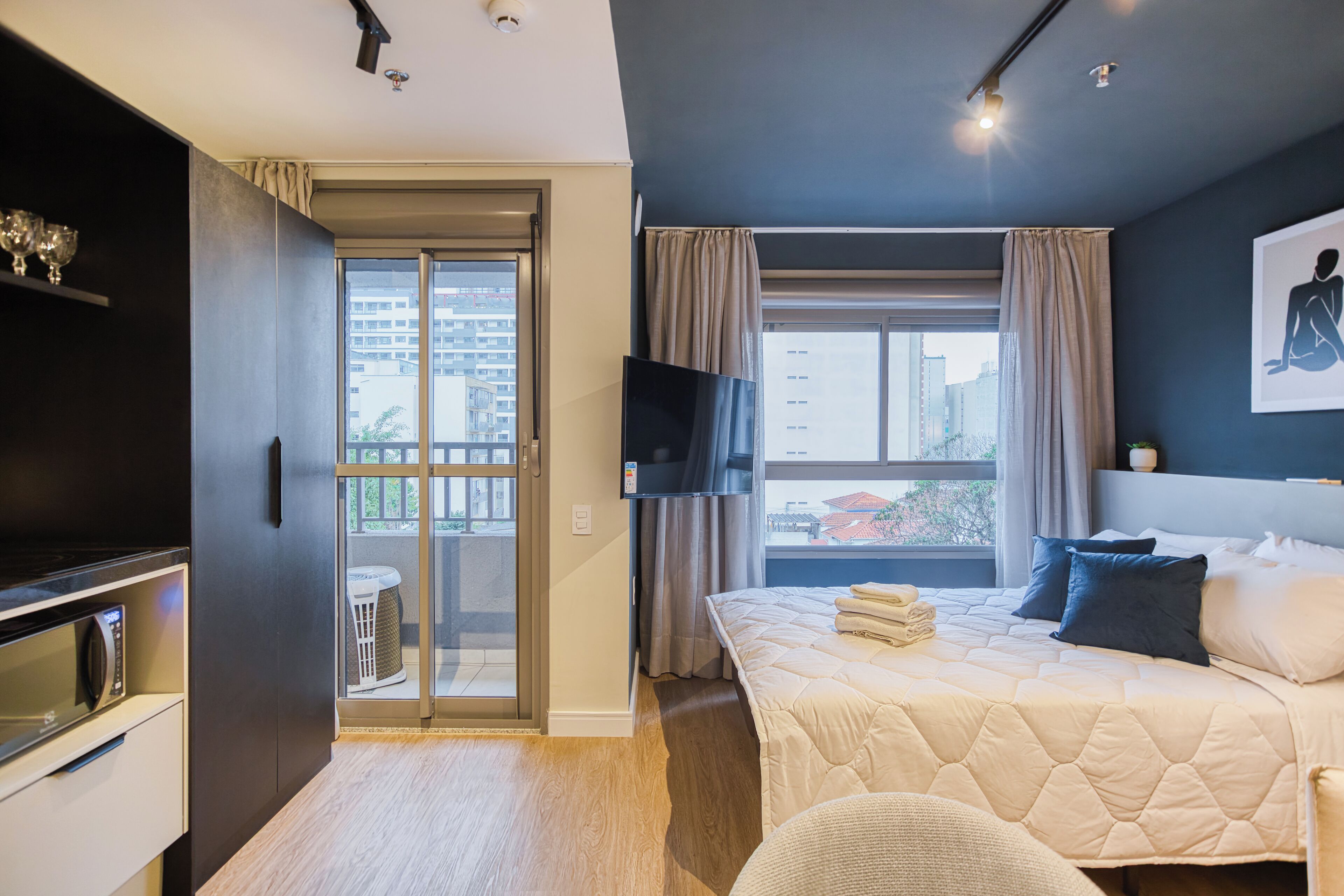 Una habitación de hotel moderna con cama, televisor de pantalla plana, balcón con puerta corredera y vistas de la ciudad.