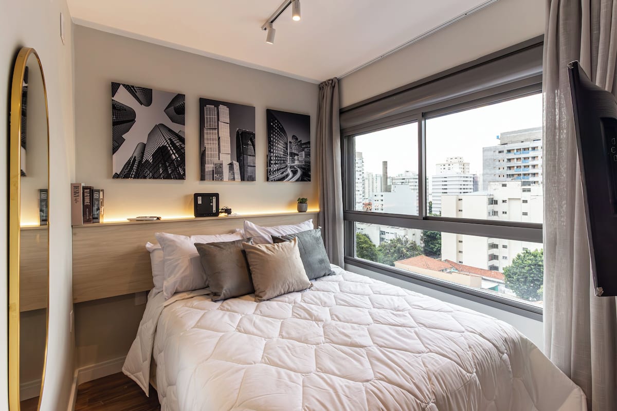 A modern bedroom with a large bed, cityscape view, and artwork on the wall.