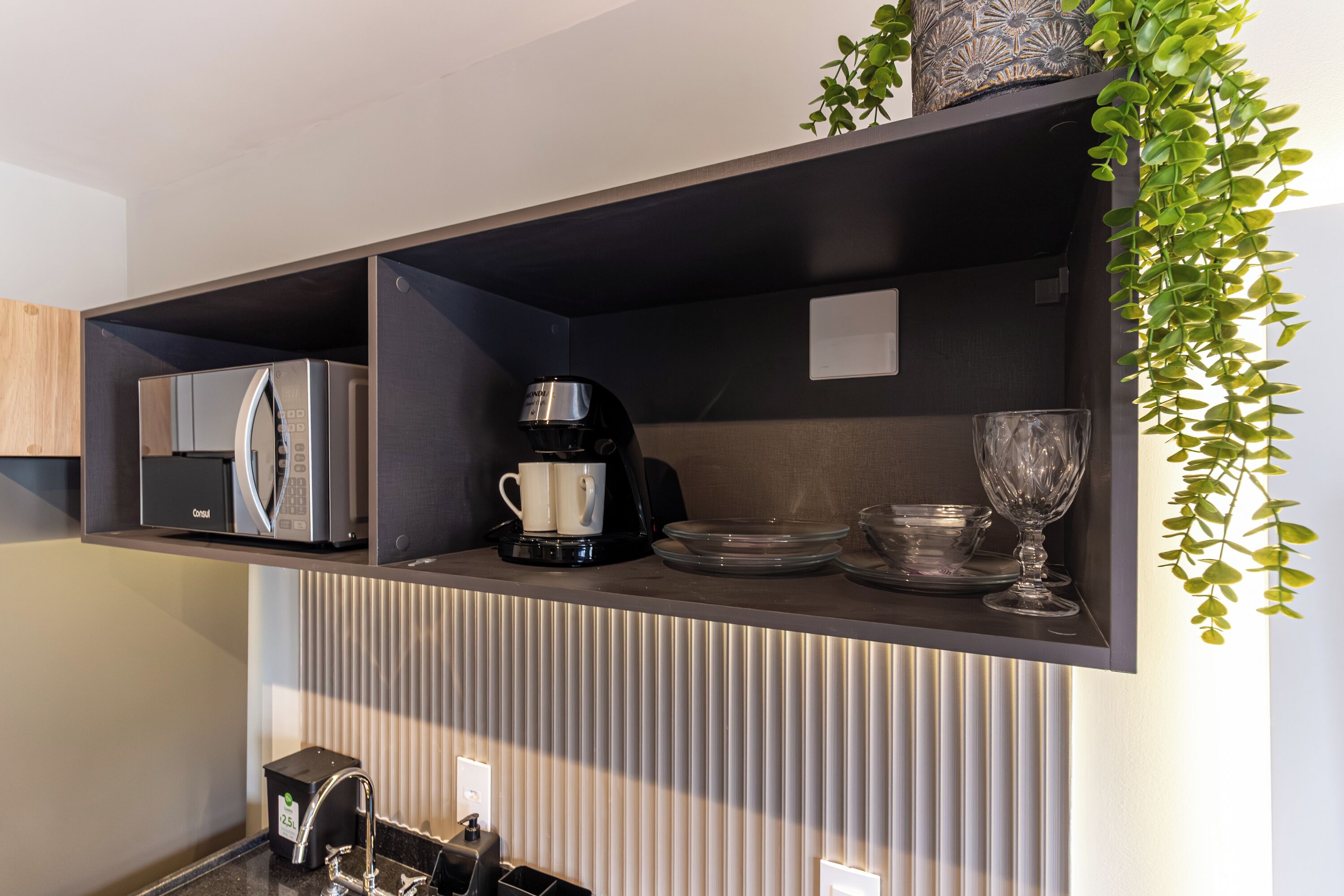 Una cocina equipada con refrigerador, cafetera y cristalería en estantes.