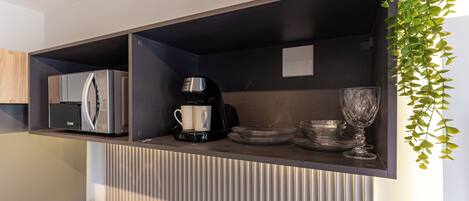 Una cocina equipada con refrigerador, cafetera y cristalería en estantes.